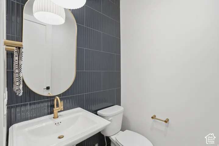Vertical dark blue textured tile accent wall, oval wall-mounted mirror with a metallic frame, pedestal sink with a metallic faucet, and matching metallic hardware fixtures