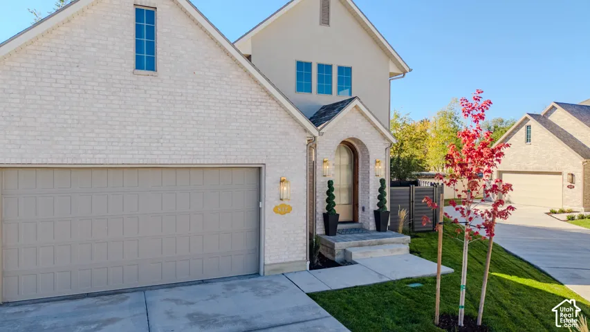 Light-colored brick facade, arched entryway, attached two-car garage, concrete driveway, and covered porch steps