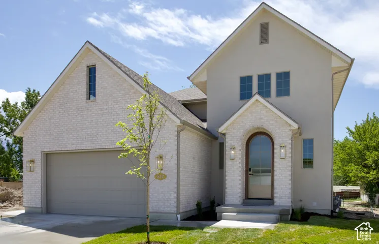 Exterior facade featuring light-toned brick and stucco siding, arched entryway, multi-gabled roofline, and an attached two-car garage