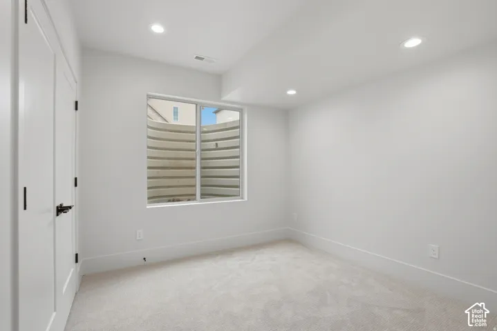 Neutral-toned carpeted flooring, inset ceiling lighting, and a slider window featuring a corrugated window well