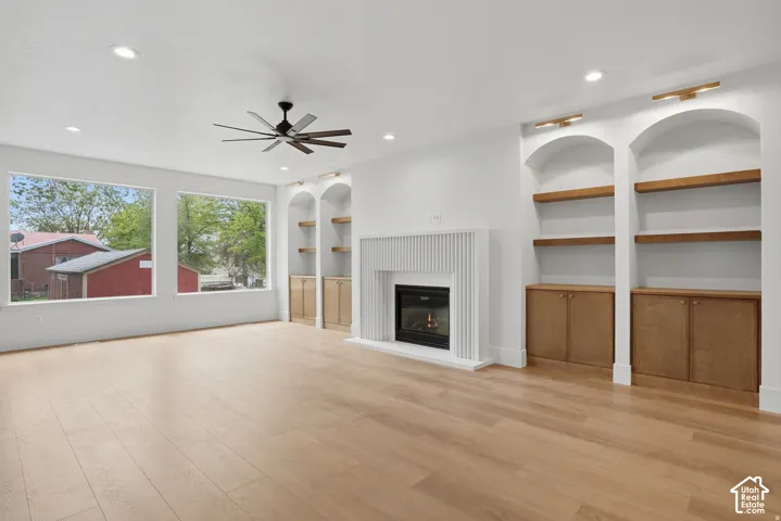 Living area featuring wood-finish flooring, recessed lighting, a fireplace with a fluted surround, and arched built-in cabinetry with wood shelving