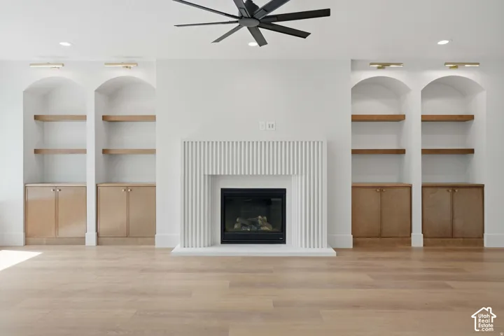 Fireplace featuring a fluted surround, flanked by custom cabinetry with arched recessed shelving and wood-finish lower storage, recessed ceiling lighting, and a multi-blade ceiling fan