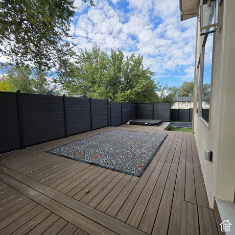 Outdoor deck featuring composite decking, a dark-toned privacy fence, and a built-in hot tub