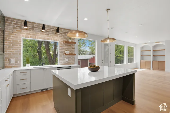 Kitchen featuring an expansive center island with stone countertop, exposed brick accent wall, wood-finish flooring, custom built-in cabinetry with integrated shelving, and recessed lighting