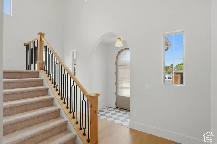 Staircase featuring carpeted steps, wooden handrail, and black metal balusters, arched entryway with a glass-paned door, high ceilings, checkerboard tile flooring, and multi-paned windows
