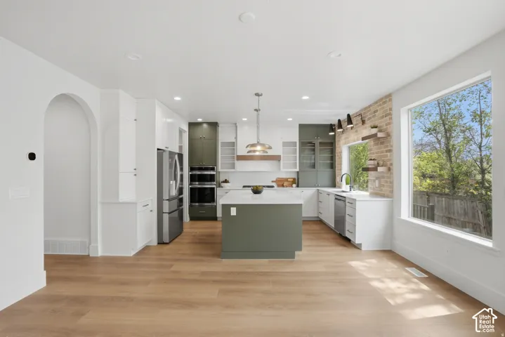 Kitchen featuring dual-tone cabinetry, a central island with a solid surface countertop, wood-finish flooring, a brick accent wall, and integrated stainless steel double wall ovens