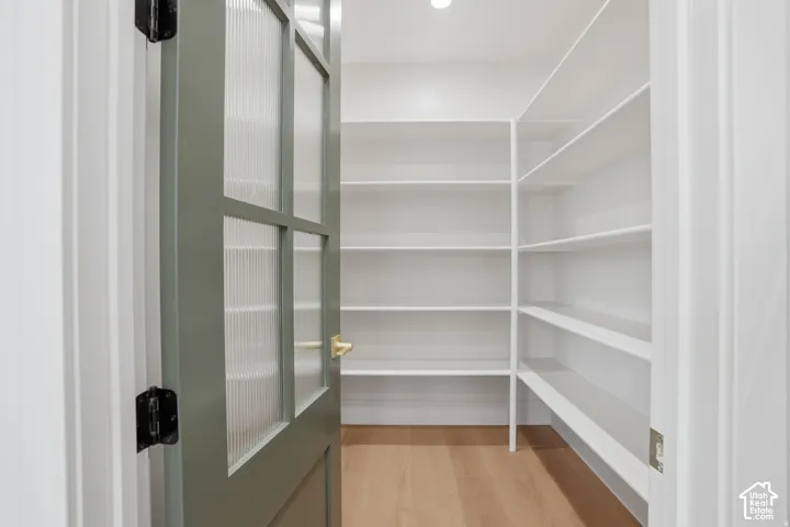 Walk-in storage space featuring custom white shelving, wood-finish flooring, and a sage-toned door with reeded glass panels