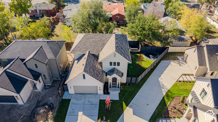 Aerial perspective of a multi-story residence featuring light-toned siding, a steep-pitched asphalt shingle roof, a two-car garage, concrete driveway, and a fenced backyard