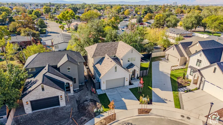 Aerial perspective of a multi-level suburban residence featuring a multi-gabled roofline, light-toned exterior siding, attached multi-car garage, and concrete driveway