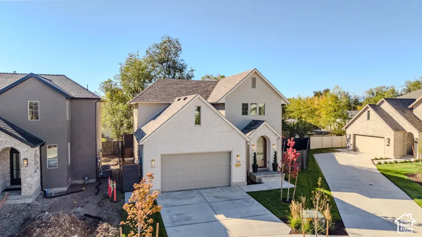 Two-story residence featuring a mixed-material exterior of light-toned brick and siding, a multi-gabled roofline, an attached two-car garage, and a concrete driveway