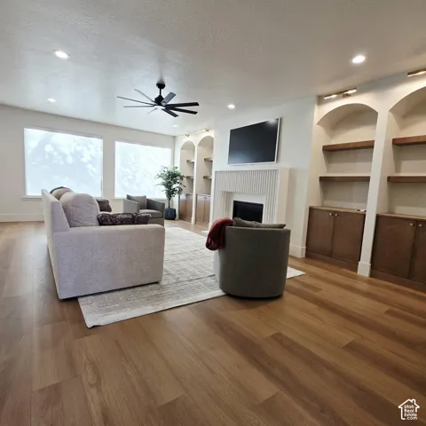 Living area featuring wood-finish flooring, a vertical-slat fireplace surround, recessed lighting, and custom built-in cabinetry with arched shelving