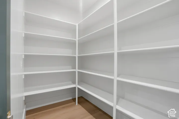 Walk-in pantry featuring white wrap-around shelving and wood-finish flooring