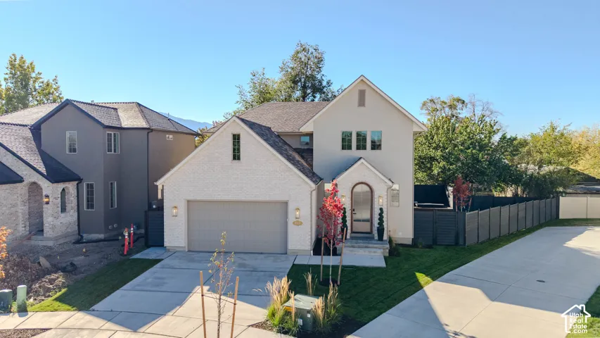 Multi-story exterior featuring a brick and stucco facade, an attached two-car garage, arched front entryway, and a concrete driveway