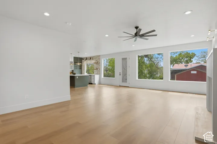Open-concept interior featuring wood-finish flooring, recessed lighting, a modern ceiling fan, large windows, and a stone-accented kitchen wall