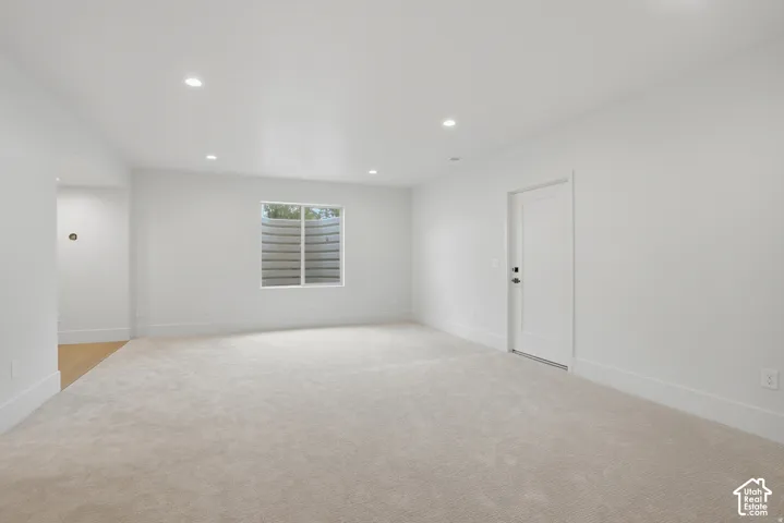 Neutral-toned interior space featuring recessed ceiling lighting, wall-to-wall carpeting, a window with an integrated egress well, and a paneled door