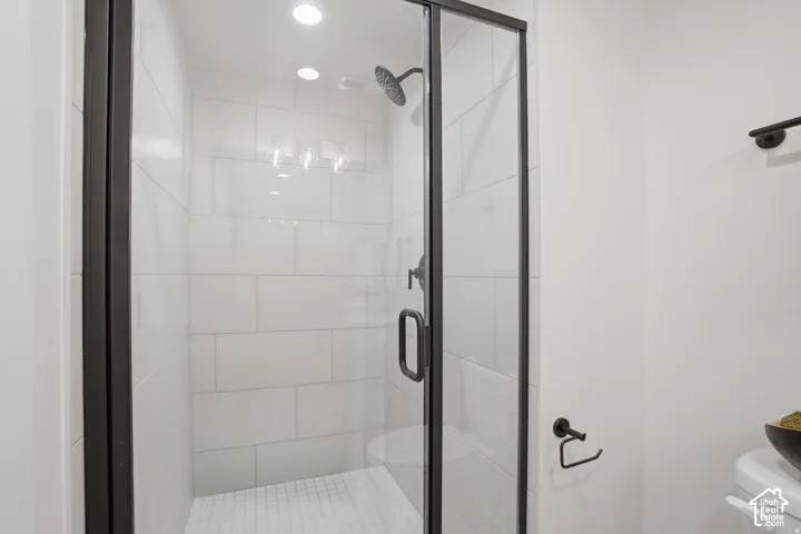 Walk-in shower featuring large-format white tile, matte black hardware, a rainfall shower head, and a glass enclosure with a black metal frame