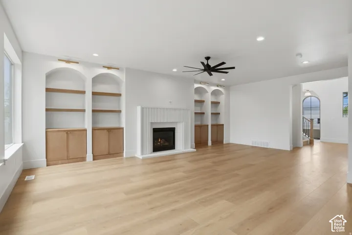 Living area featuring wood-finish flooring, a vertical-slat fireplace surround, recessed lighting, and dual arched built-in shelving units with lower cabinetry