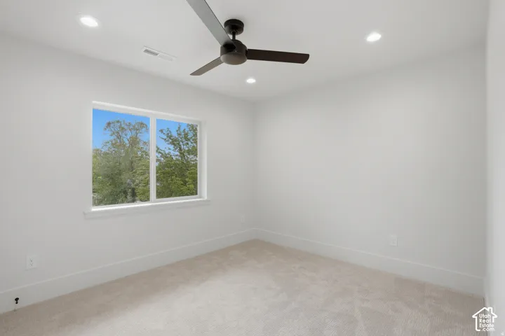 Neutral-toned interior room featuring wall-to-wall carpeting, recessed ceiling lighting, a matte black ceiling fan, and a large window