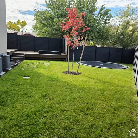 Backyard featuring a raised composite deck, perimeter privacy fencing, manicured lawn, and in-ground trampoline