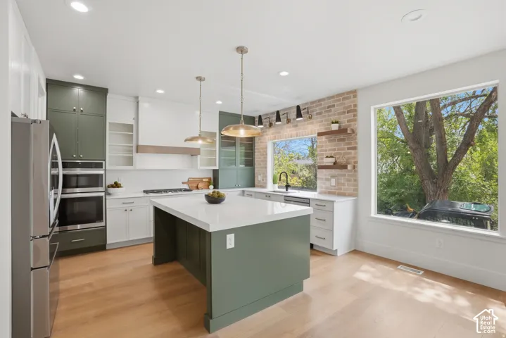 Kitchen featuring a central island with a quartz countertop, olive-toned cabinetry, light wood-finish flooring, a brick accent wall, and double wall ovens