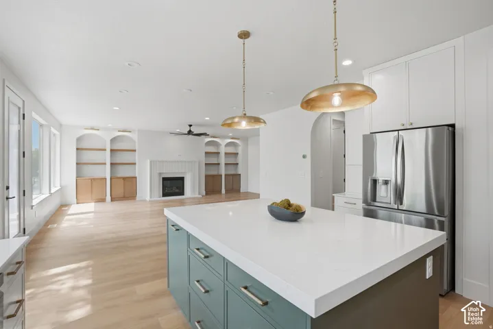 Kitchen island with a solid-surface countertop and integrated cabinetry, wood-finish flooring, dual metal pendant lighting, built-in recessed shelving, and a gas fireplace with a decorative mantel