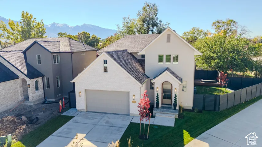 Two-story residence featuring a combination brick and stucco exterior, arched front entryway, multi-gabled roofline, concrete driveway, and mountain backdrop