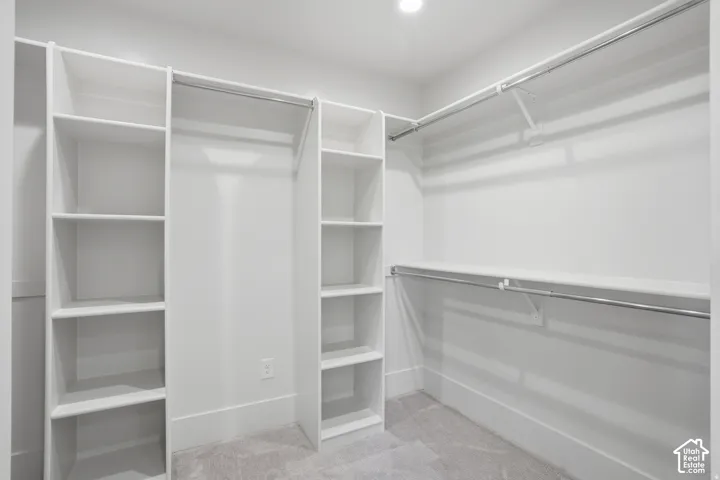 Walk-in closet featuring white built-in shelving, multiple tiered hanging rods, and neutral carpeting