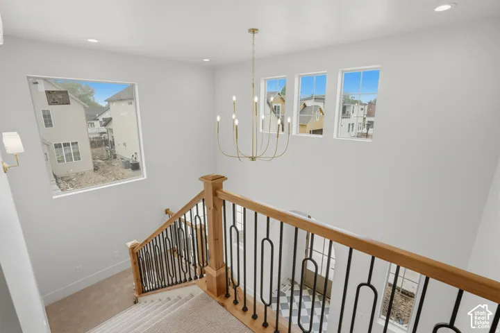 High-ceilinged entry featuring a multi-light brass chandelier, wood-topped railing with black metal balusters, and expansive windows