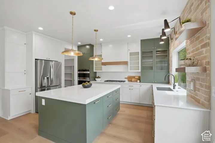 Kitchen featuring a central island with quartz countertops, custom cabinetry in dual tones, integrated stainless steel appliances, wood-finish flooring, and a brick-accented wall with floating shelving