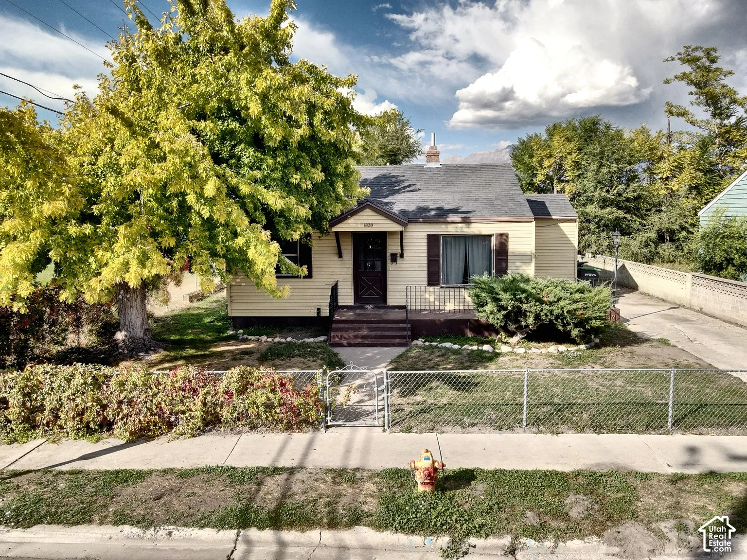 Single-story residence with light-colored siding, a dark-toned roof, and a front porch featuring a metal railing