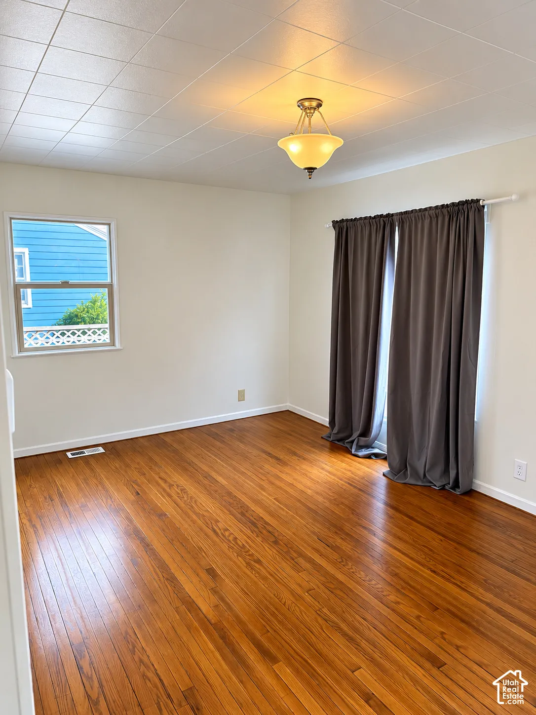 Hardwood flooring, neutral wall tones, decorative ceiling light fixture, and a window with natural light