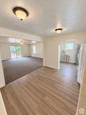 Wood-finish flooring leading to a carpeted living area with a ceiling fan