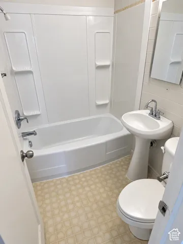 Pedestal sink, white toilet, and tub-shower combination with white surround