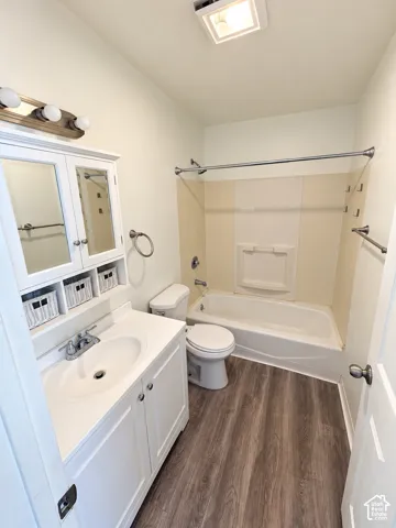 Bathroom featuring wood-finish flooring, a white vanity with an integrated sink, a built-in medicine cabinet, a full bathtub, and a shower with a shower curtain rod