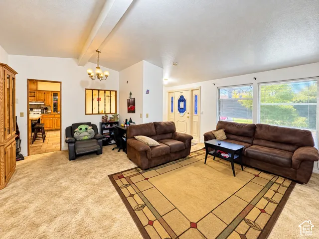Vaulted ceilings, carpeted flooring, multi-pane front entry door, inset interior window, and suspended chandelier lighting
