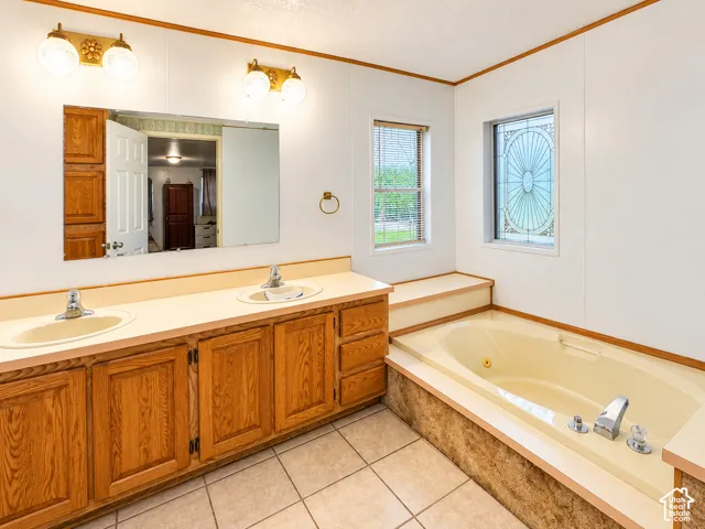 Double vanity featuring light-toned integrated sinks, wood cabinetry, a large wall-mounted mirror, dual globe-style light fixtures, and a soaking tub with decorative leaded glass window accent