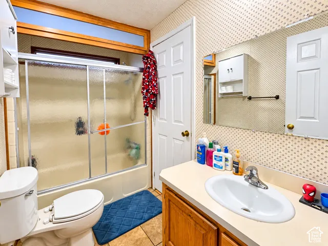 Bathroom featuring a shower-tub combination with sliding glass doors, wooden vanity with integrated sink, large wall-mounted mirror, and overhead cabinet storage