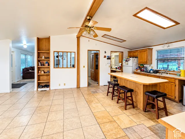 Open-concept kitchen featuring an expansive center island with seating, built-in wooden shelving, recessed skylights, and tile flooring