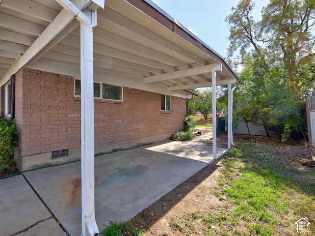 Covered patio with a concrete surface, brick exterior, and a partially grassed yard area