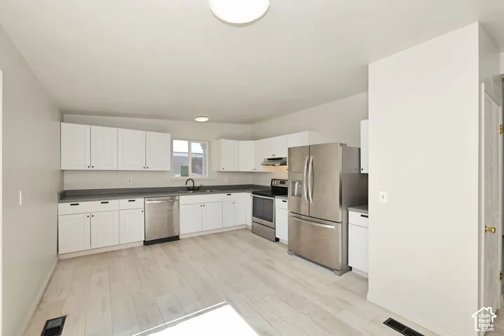 Kitchen featuring white cabinetry, wood-finish flooring, stainless steel appliances, and dark countertops