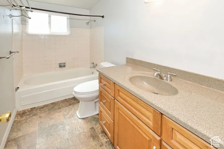 Bathroom featuring a wood-finish vanity with an integrated sink and light-toned countertop, a white bathtub with tiled surround, and patterned floor tile