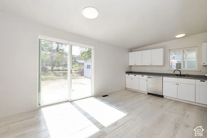 White shaker cabinetry with dark countertops, stainless steel dishwasher, and a black gooseneck faucet