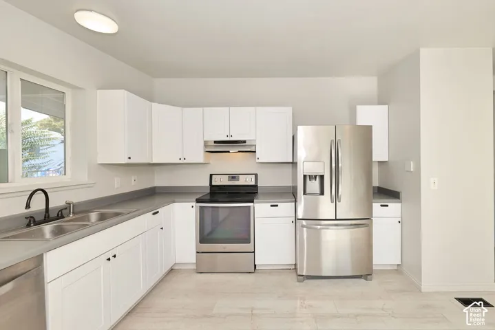 White shaker cabinetry, stainless steel appliances, dual basin sink, light-toned flooring, and counter space