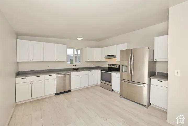 Kitchen featuring white shaker cabinetry, stainless steel appliances, dark countertops, and wood-finish flooring