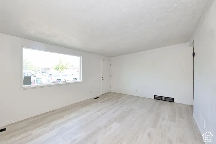 Bright, open room featuring pristine wood-finish flooring, abundant natural light from a large horizontal window, and clean white walls with fresh finishes