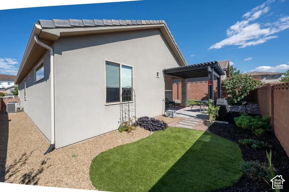 Stucco exterior featuring a covered pergola, concrete patio, synthetic turf area, and perimeter masonry fencing