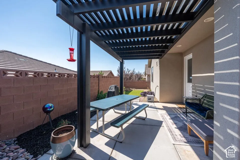 Covered patio featuring a black metal pergola, concrete flooring, and a decorative concrete block perimeter wall