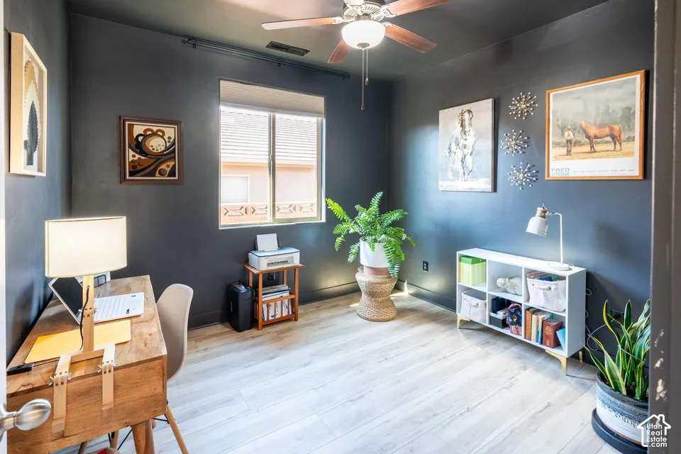 Room featuring wood-finish flooring, single-pane window with roller shade, and ceiling fan with integrated light fixture
