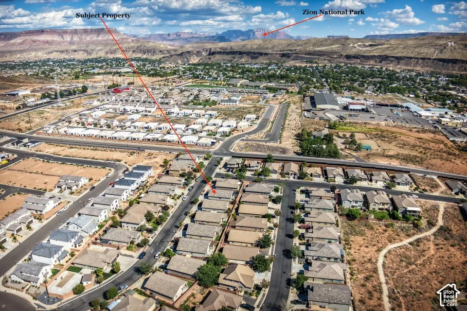 Aerial perspective of a residential neighborhood featuring paved streets, grid-patterned housing layouts, and distant mountain topography
