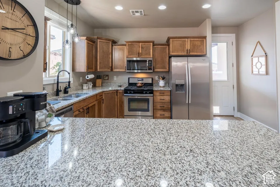 Kitchen featuring stone-finish countertops, stainless steel appliances, wood cabinetry, recessed lighting, and a dual-basin sink with a matte black faucet